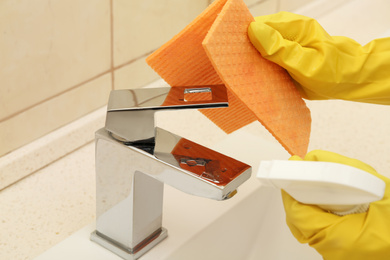 Photo of Person cleaning faucet with rag and detergent in bathroom, closeup