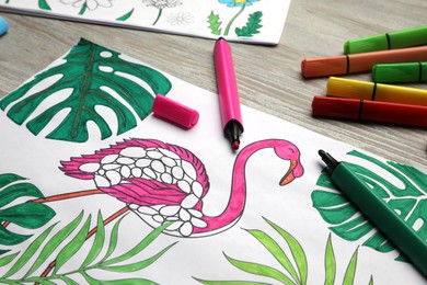 Photo of Coloring page with children drawing and set of felt tip pens on wooden table, closeup