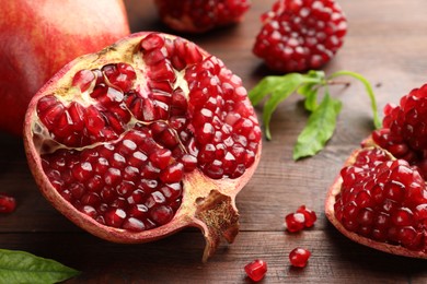 Photo of Cut fresh pomegranate and green leaves on wooden table, closeup