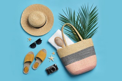 Photo of Wicker bag, camera, palm leaves and beach accessories on light blue background, flat lay