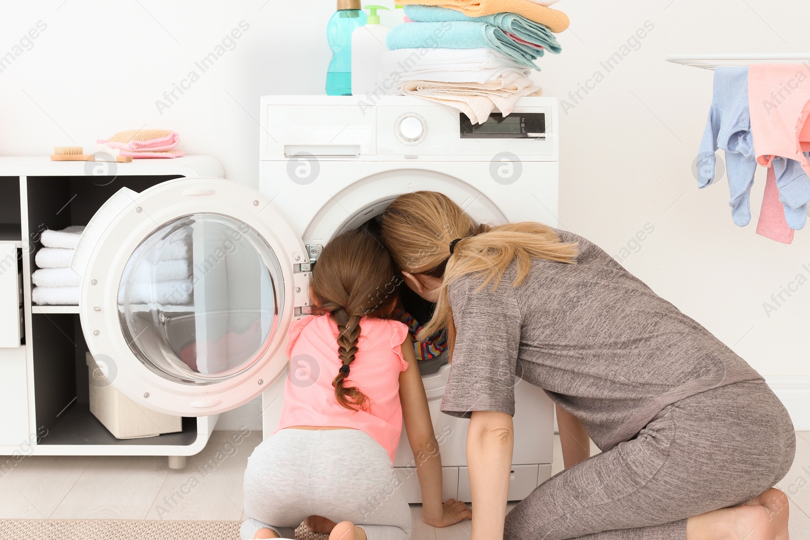 Photo of Housewife with little daughter doing laundry at home