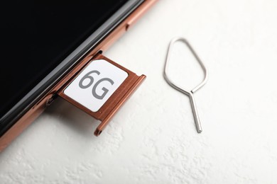 Internet concept. 6G SIM card in tray and smartphone on white table, closeup