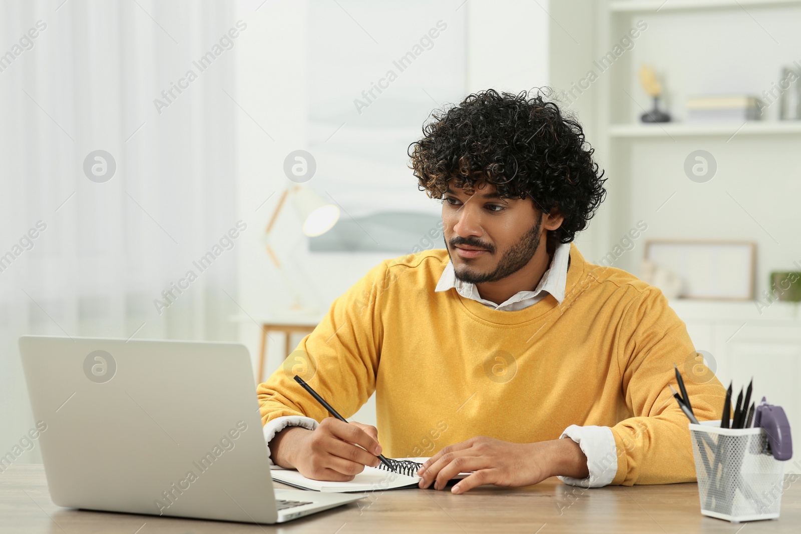 Photo of Handsome man taking notes near laptop in room