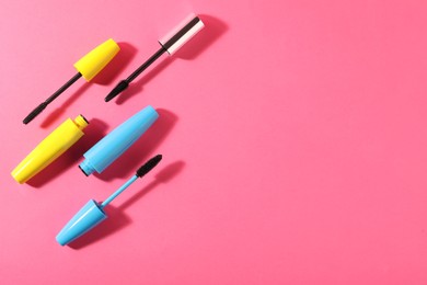 Different mascaras on bright pink background, flat lay. Space for text