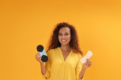 Photo of Young African American woman with reusable menstrual pad and pantyliner on yellow background.