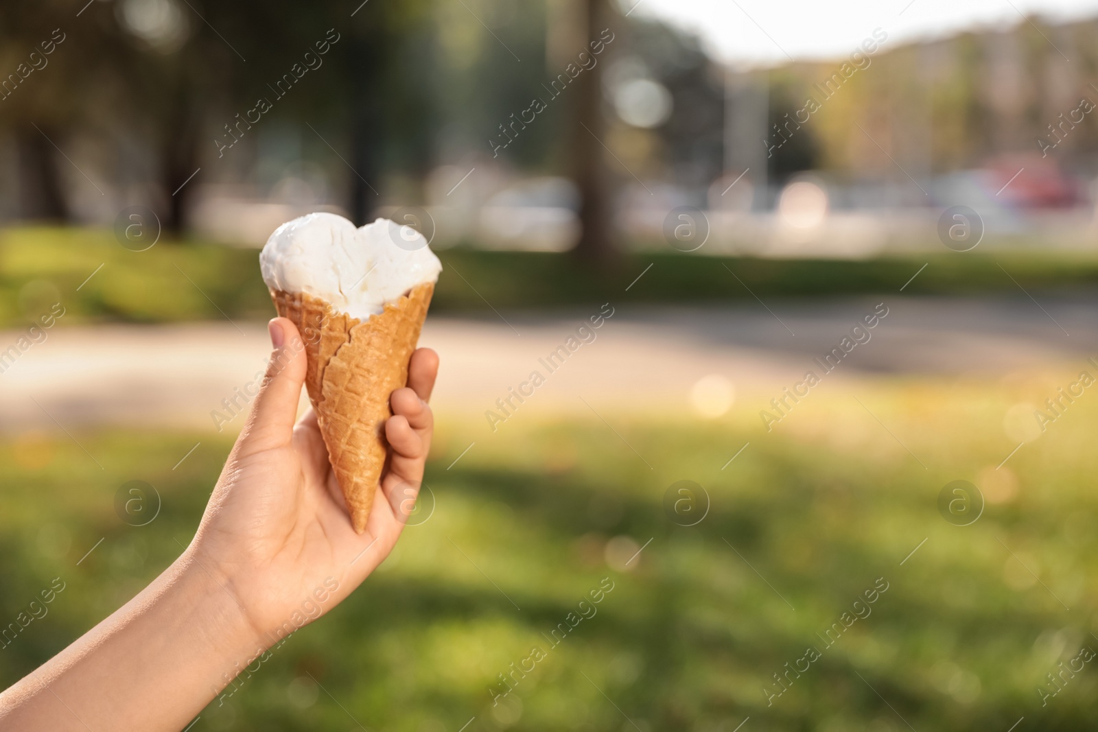 Photo of Woman holding delicious ice cream in waffle cone outdoors, closeup of hand. Space for text