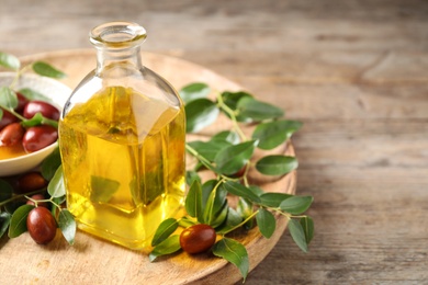 Glass bottle with jojoba oil and seeds on wooden table. Space for text