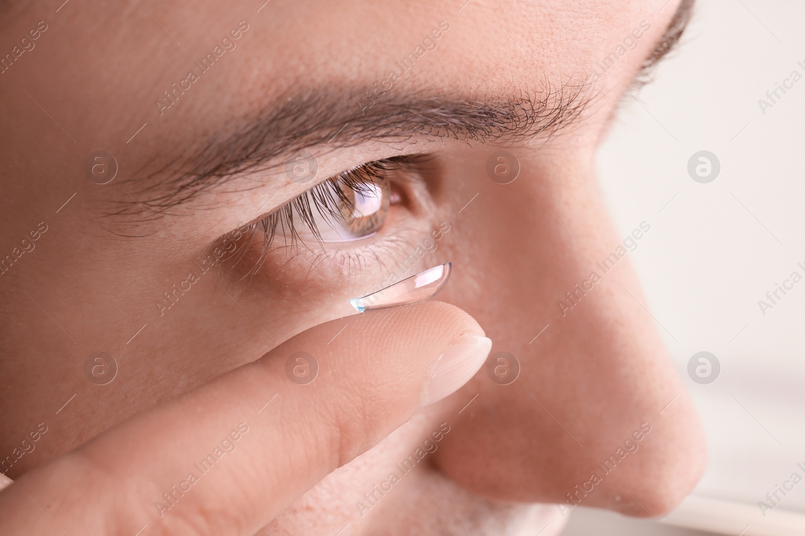 Photo of Young man putting contact lens in his eye, closeup