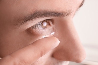 Photo of Young man putting contact lens in his eye, closeup