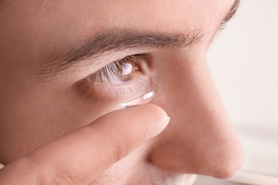 Young man putting contact lens in his eye, closeup