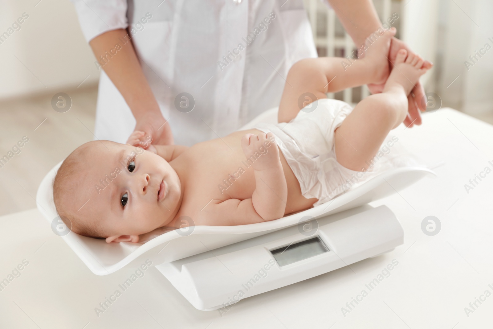 Photo of Doctor weighting baby on scales in light room