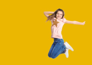 Cute girl jumping on golden background, space for text