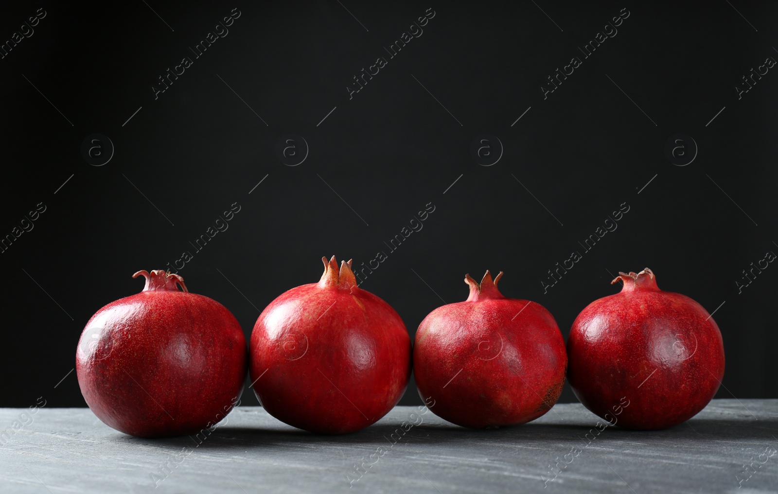 Photo of Ripe pomegranates on table against black background, space for text