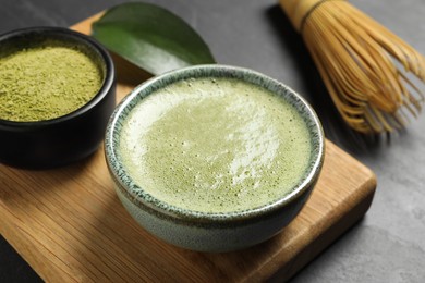 Photo of Cup of fresh matcha tea, bamboo whisk and green powder on black table, closeup