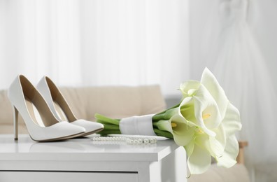 Beautiful calla lily flowers tied with ribbon, shoes and jewelry on white chest of drawers indoors