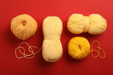 Soft woolen yarns on red background, flat lay