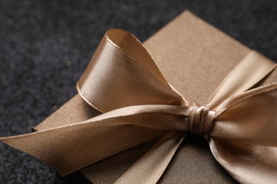 Photo of Shiny gift box with golden bow on black background, closeup