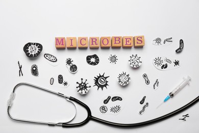 Photo of Word Microbes made with wooden cubes, pictures, syringe and stethoscope on white background, flat lay