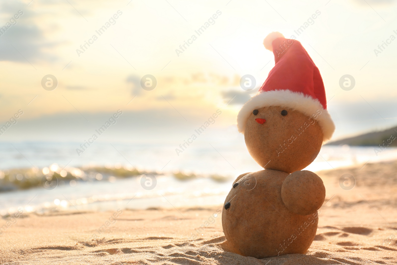 Photo of Snowman made of sand with Santa hat on beach near sea, space for text. Christmas vacation