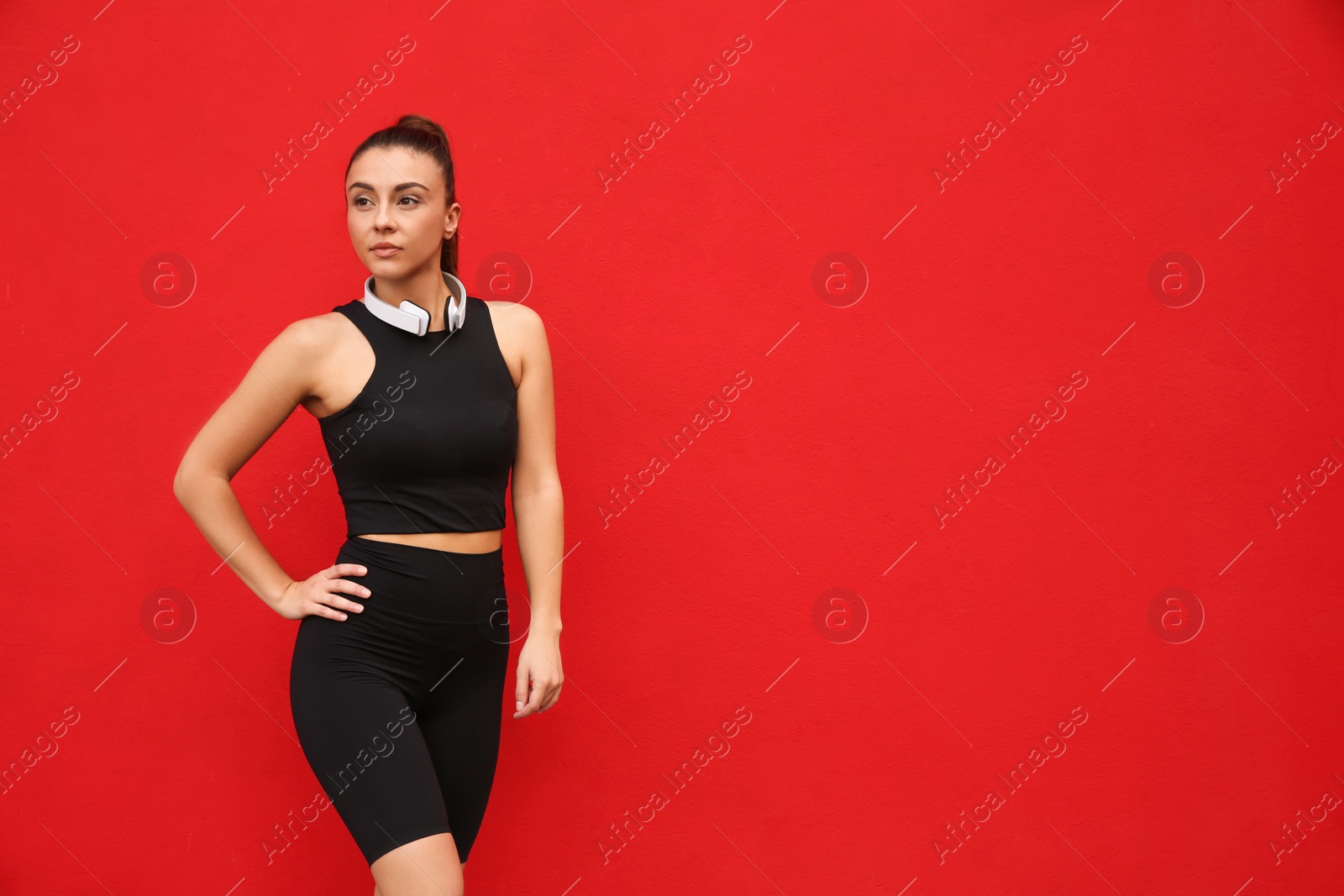 Photo of Young woman in sportswear with headphones on red background. Space for text