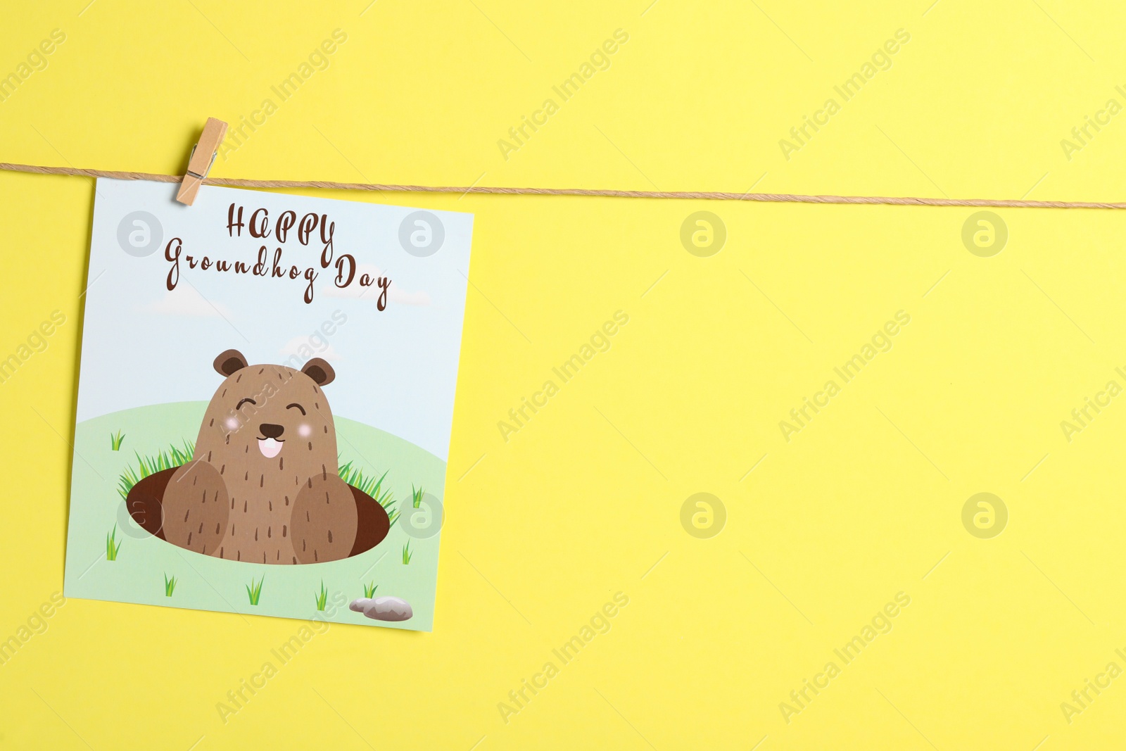 Photo of Happy Groundhog Day greeting card hanging on yellow background, space for text