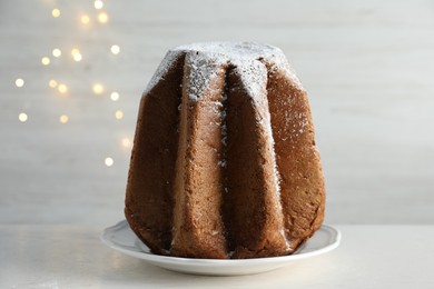 Photo of Delicious Pandoro cake decorated with powdered sugar on white table. Traditional Italian pastry