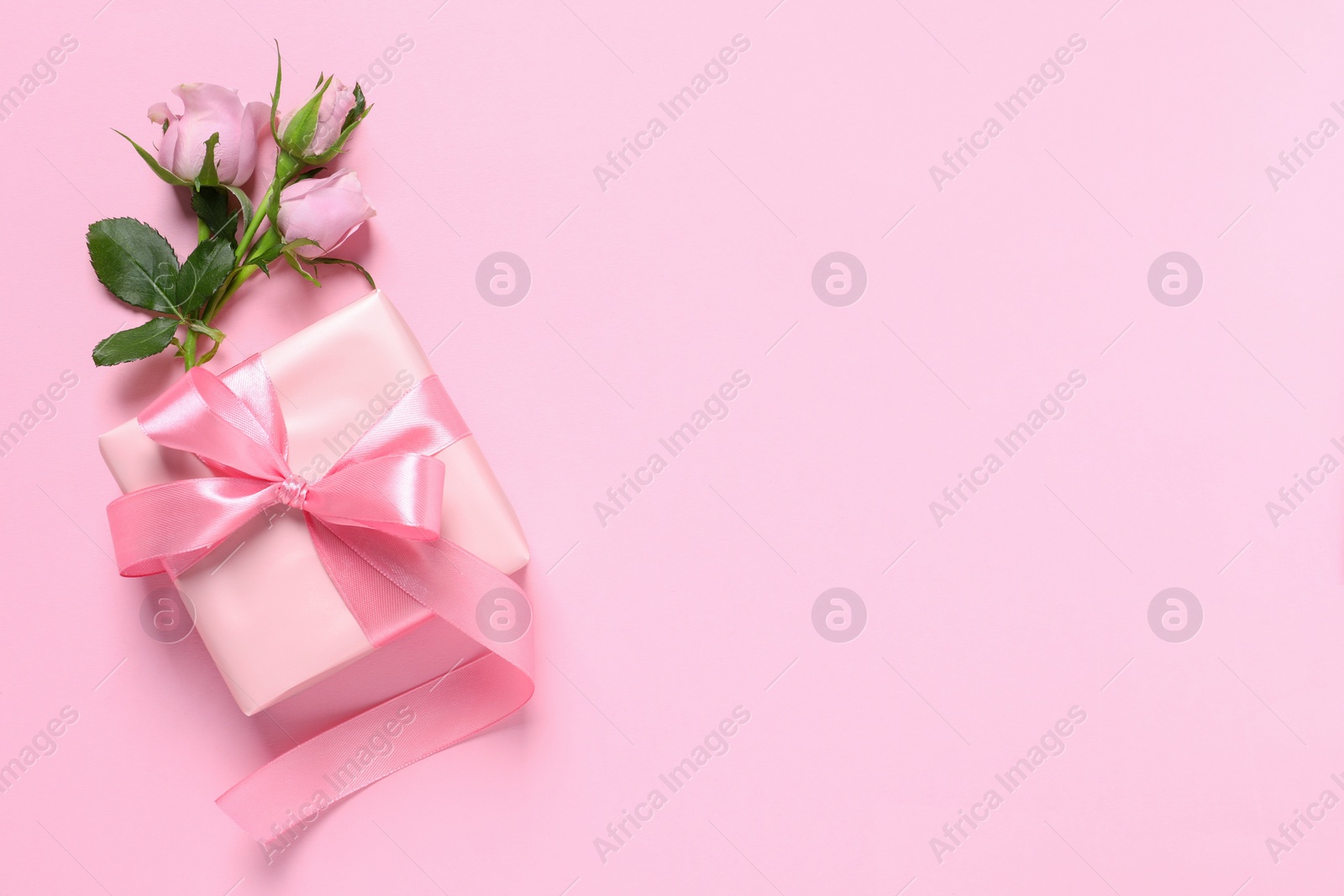 Photo of Gift box and beautiful rose flowers on pink background, flat lay. Space for text