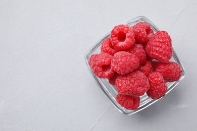 Photo of Delicious fresh ripe raspberries in glass bowl on grey table, top view. Space for text