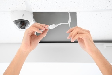 Photo of Technician installing CCTV camera on ceiling indoors, closeup