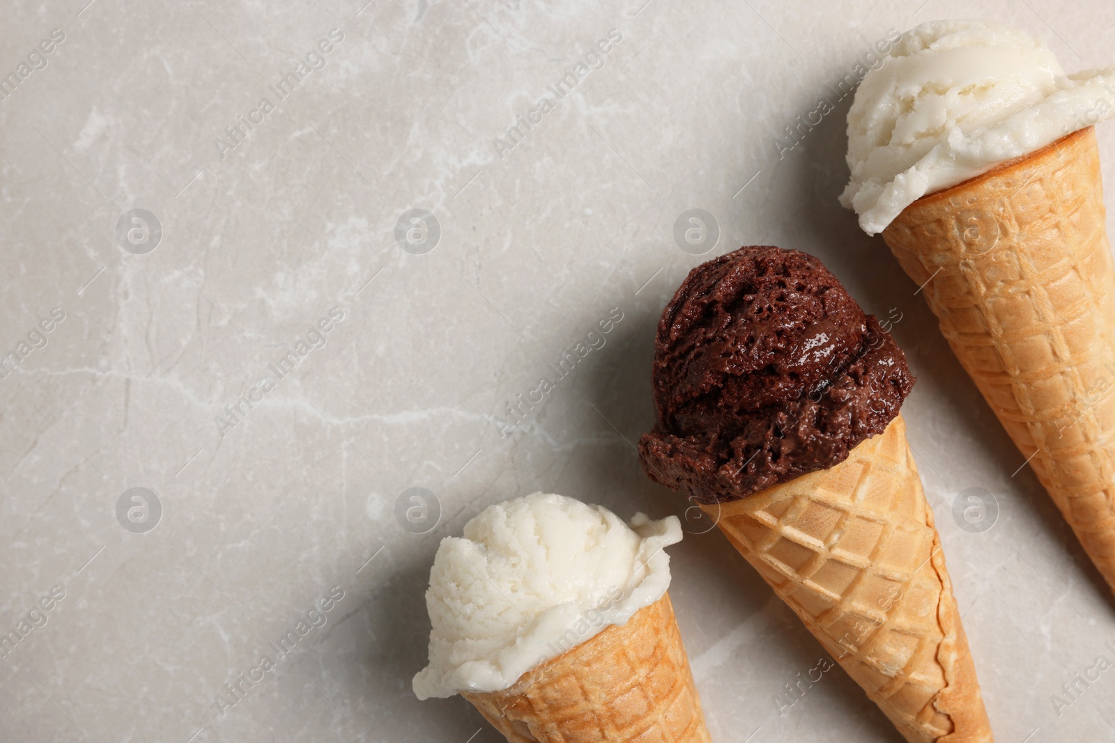 Photo of Tasty ice cream scoops in waffle cones on light marble table, flat lay. Space for text