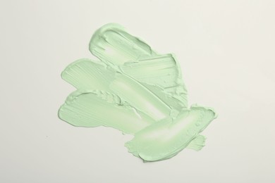 Photo of Strokes of green color correcting concealer on white background, top view
