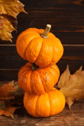 Photo of Stack of fresh ripe pumpkins and dry leaves on wooden table