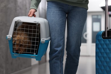 Photo of Travel with pet. Woman with suitcase holding carrier with dog indoors, closeup