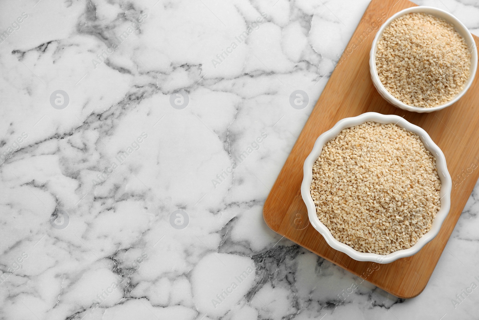 Photo of Sesame seeds on white marble table, top view. Space for text