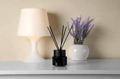 Photo of Aromatic reed air freshener, lamp and lavender flowers on white table indoors