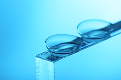 Photo of Pair of contact lenses on glass against light blue background, closeup. Space for text