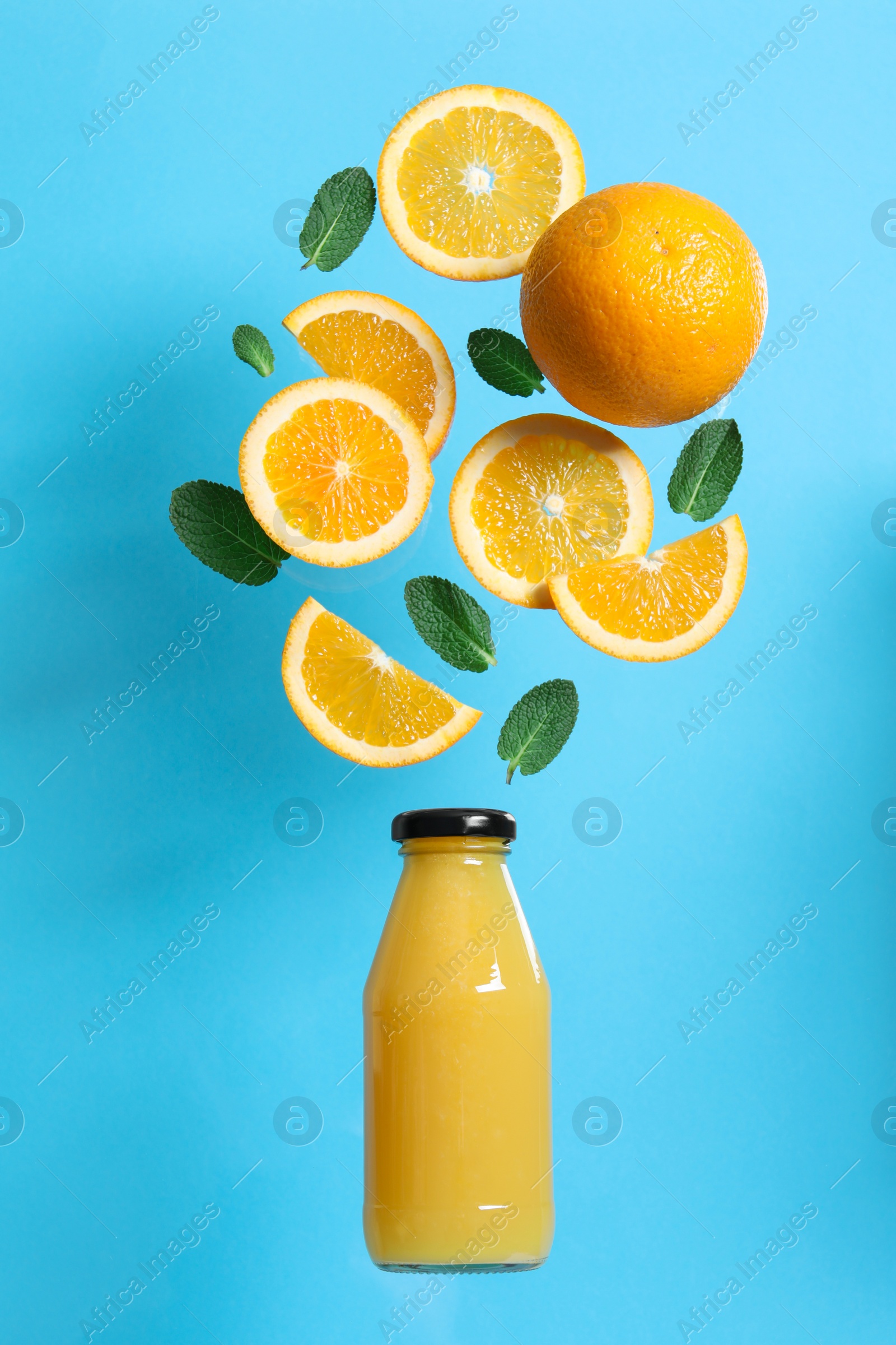 Photo of Tasty ripe oranges and green leaves over glass bottle on light blue background