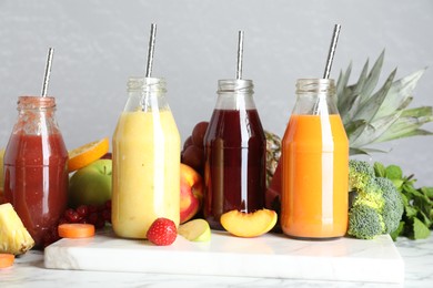 Photo of Bottles of delicious juices and fresh fruits on white marble table