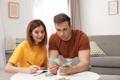 Photo of Couple counting money at table in living room