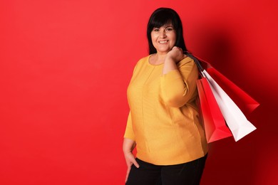Photo of Beautiful overweight mature woman with shopping bags on red background. Space for text