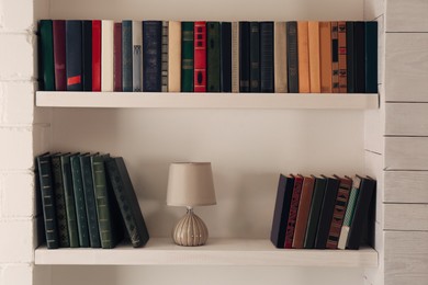 Photo of Shelves with different books and lamp on light wall