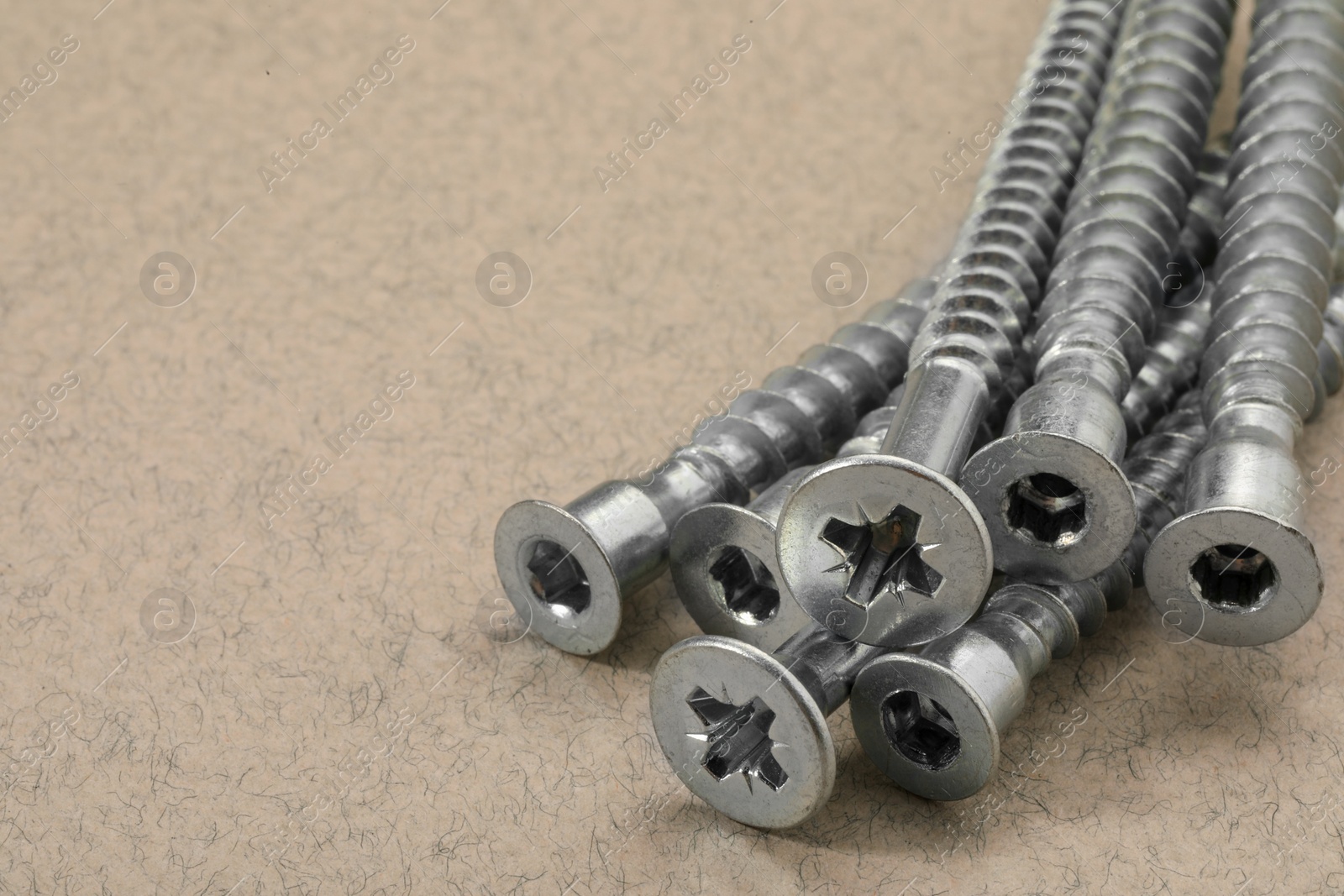 Photo of Many metal screws on beige background, closeup. Space for text