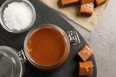 Tasty salted caramel in glass jar on grey table, flat lay