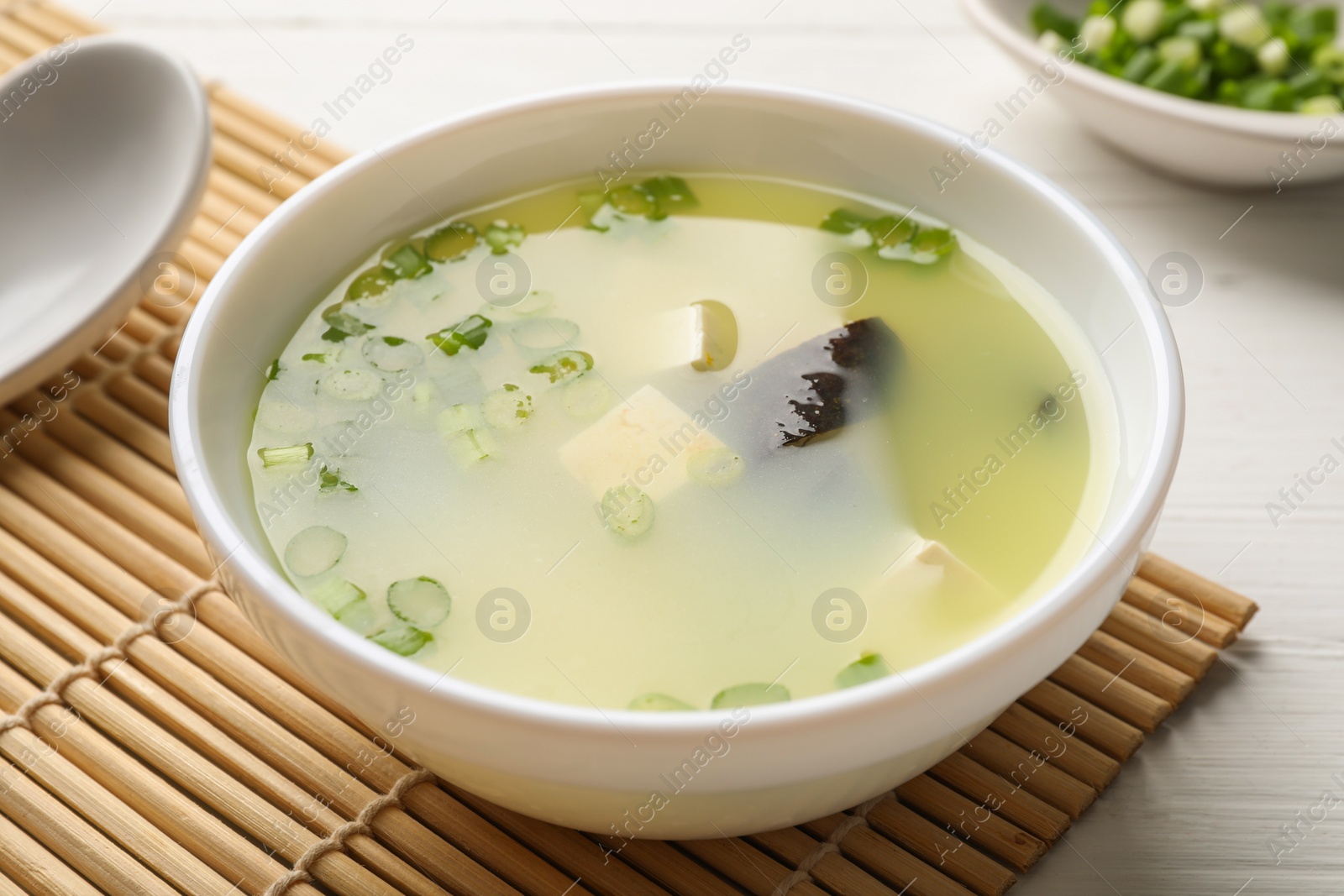 Photo of Bowl of delicious miso soup with tofu served on white wooden table, closeup