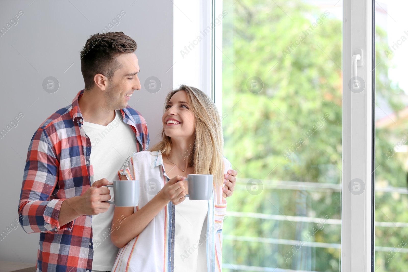 Photo of Happy young couple drinking morning coffee near window at home