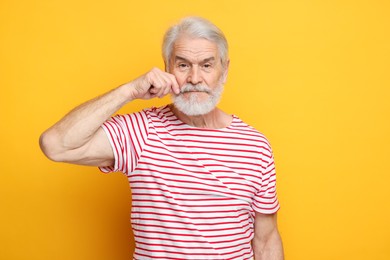 Photo of Senior man touching mustache on orange background