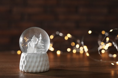 Snow globe with Christmas lights on wooden table. Space for text