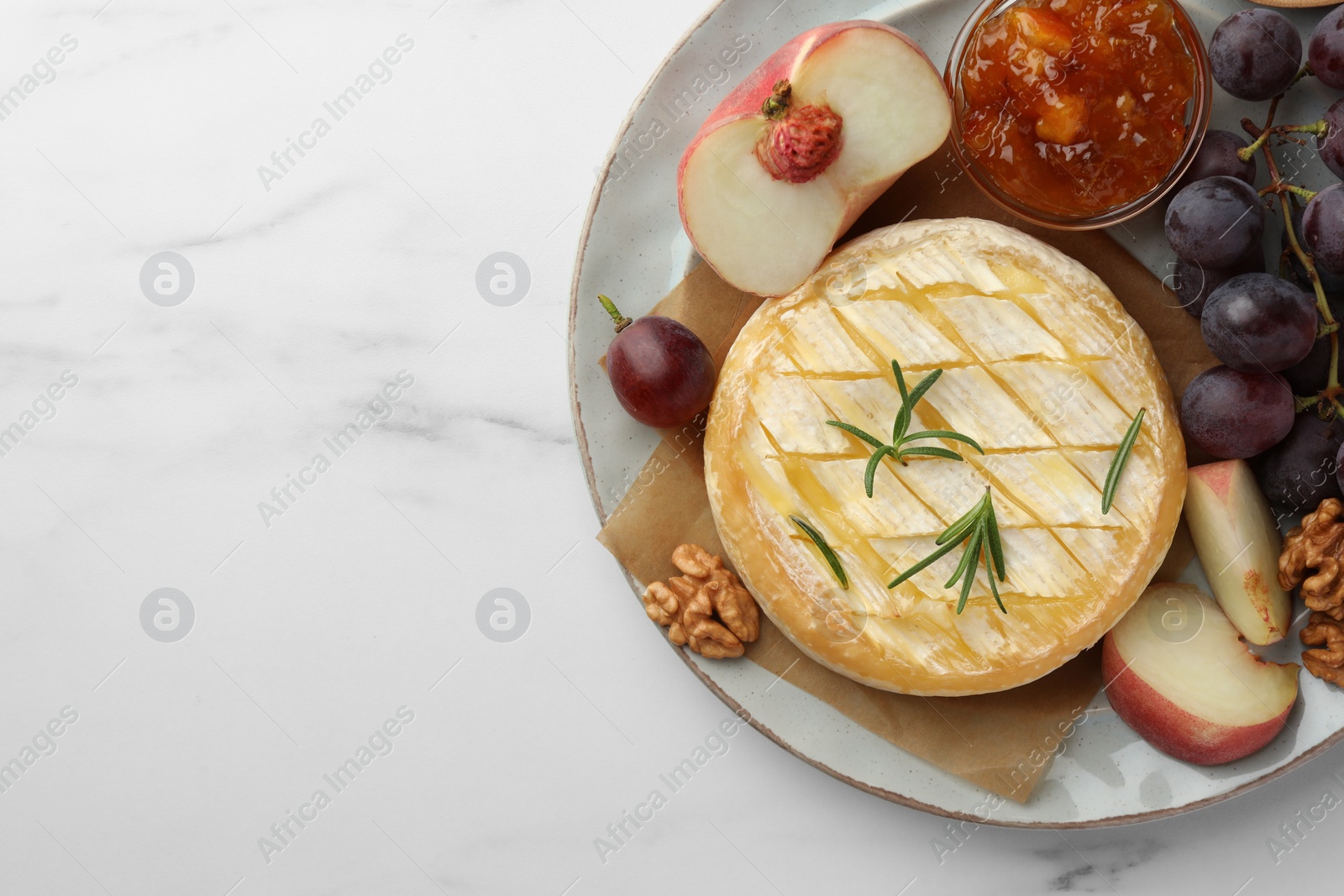 Photo of Tasty baked brie cheese served on white marble table, top view. Space for text