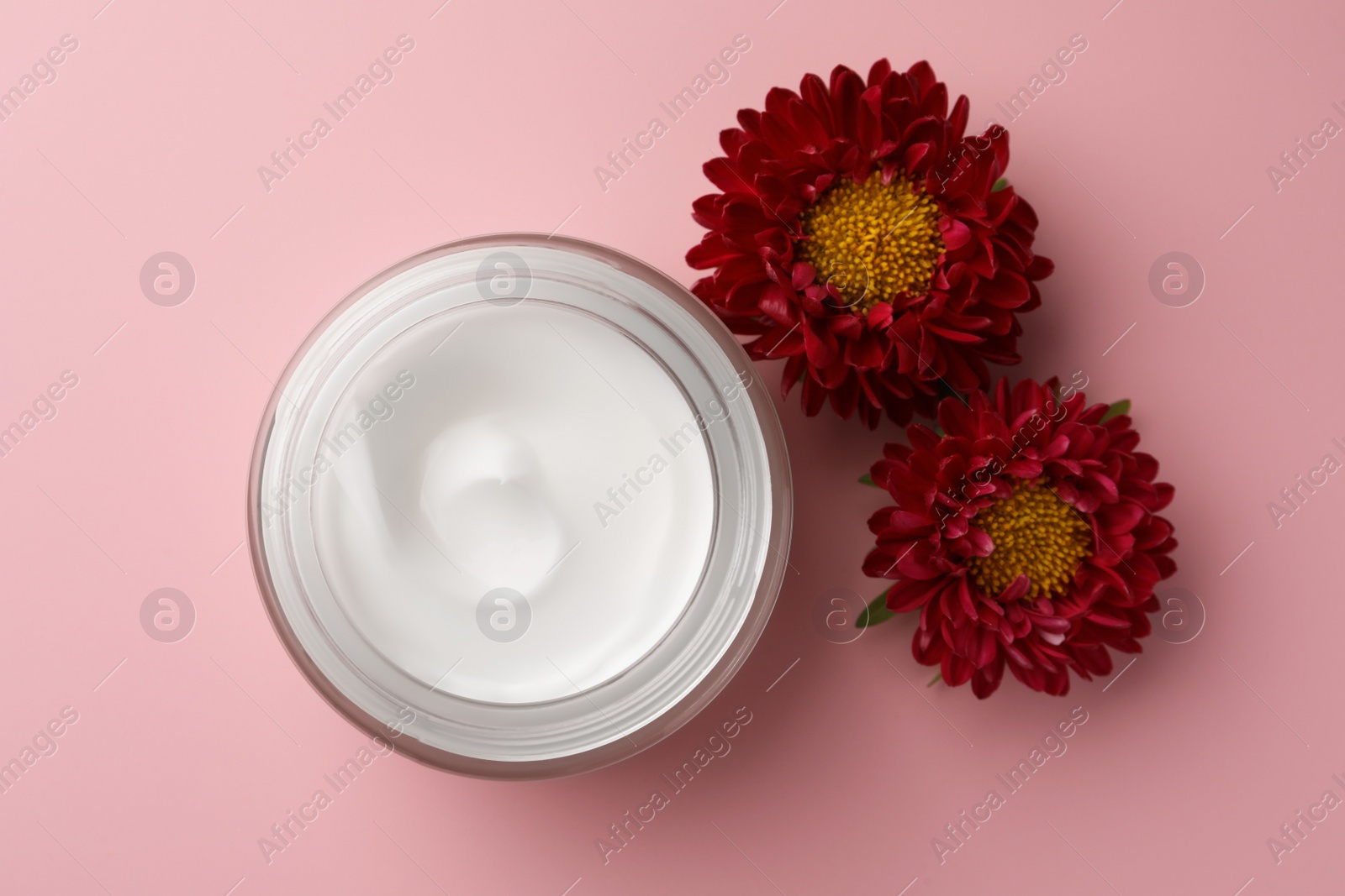 Photo of Jar of face cream and chrysanthemum flowers on pink background, flat lay