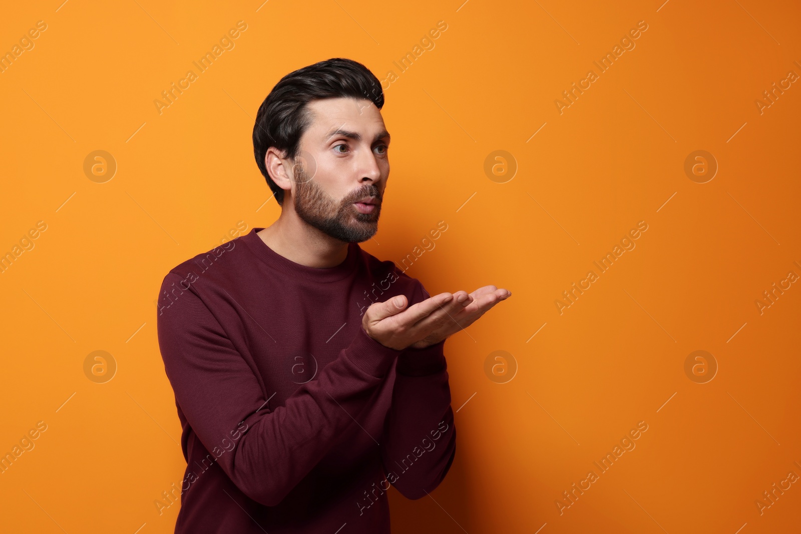 Photo of Handsome man blowing kiss on orange background. Space for text
